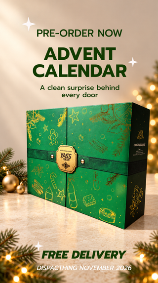 A green Christmas Advent Calendar box with gold festive illustrations, displayed on a marble surface with holiday lights and pine branches free delivery